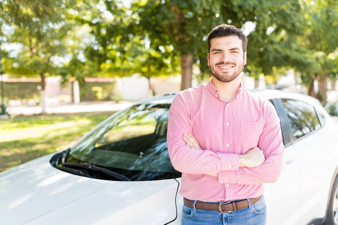 a man in a pink shirt standing in front of a car